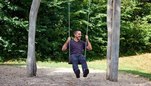A Hispanic man sitting on a swing in a park