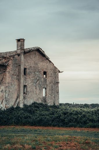 An abandoned rustic house in a lush green field under a cloudy sky, evoking a sense of nostalgia and solitude.