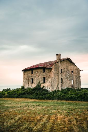 An abandoned rustic house in a grassy field under a cloudy sky, evoking a sense of nostalgia and history.