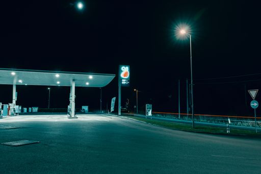 A nighttime view of an illuminated gas station with a clear sky and streetlights, creating a serene urban scene.