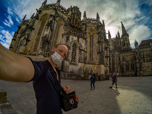 A caucasian man in a protective mask taking a selfie against the Batalha Monastery in Portugal