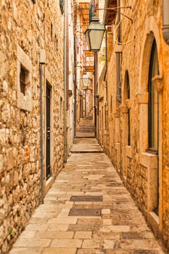 A vertical shot of an old alleyway with street lights along a building