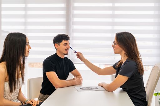 Female aesthetic medicine doctor conducting an evaluation consultation with two caucasian patients in a clean, bright clinical room.