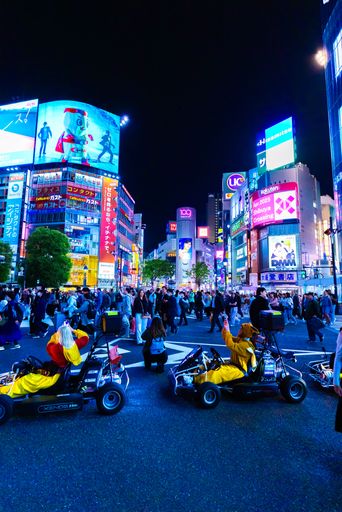 Vibrant night scene at Shibuya Crossing, Tokyo, with people in costumes driving go-karts amidst illuminated billboards.