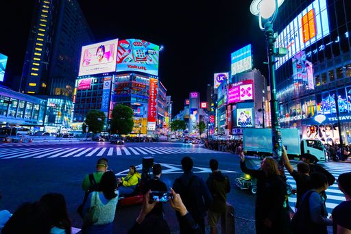 Crowds gather at the vibrant Shibuya Crossing in Tokyo at night, illuminated by bright neon lights and bustling city life.