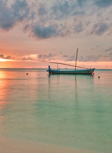 A vertical shot of a fishing boat in the ocean with the gorgeous golden sunset in the background