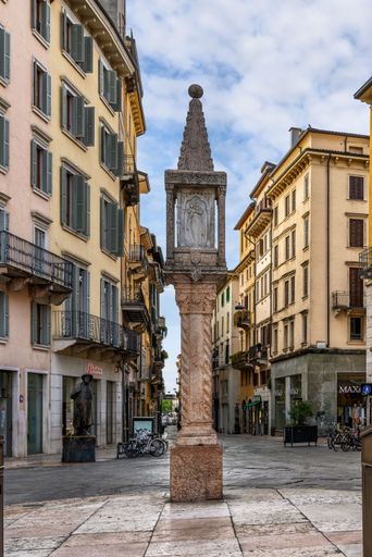 This striking image features a gothic-style monument adorned with religious sculptures, standing tall against a backdrop of classic yellow buildings.