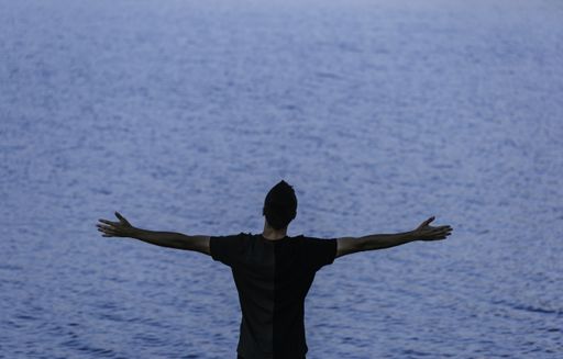 A beautiful shot of a male raising  arms up and looking to the dark blue sea