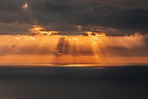 The sunbeams breaking through clouds over a calm sea at sunset, creating a serene seascape.