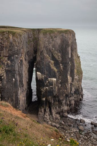 A stunning coastal cliff formation with a natural arch overlooking the sea in Pembrokeshire, Wales.