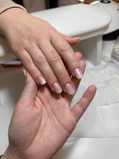 A close-up of nail technician holding client's hand with glittery nails after manicure