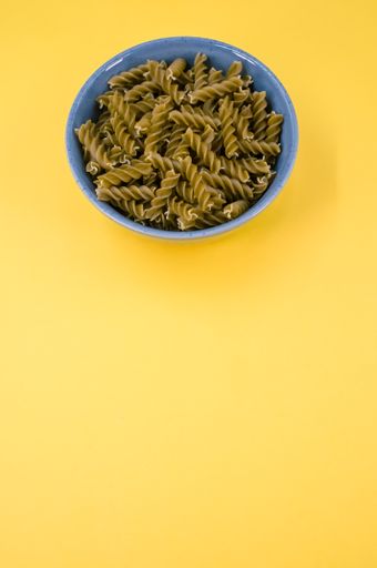 Vertical shot of  italian fusilli pasta in a blue bowl on a yellow background with text space