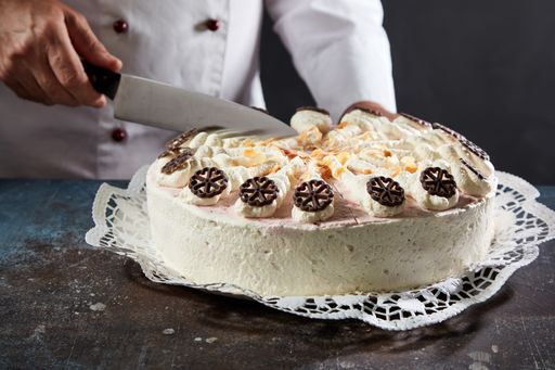 A closeup shot of a male's hands cutting appetizing white strawberry cake served on a table