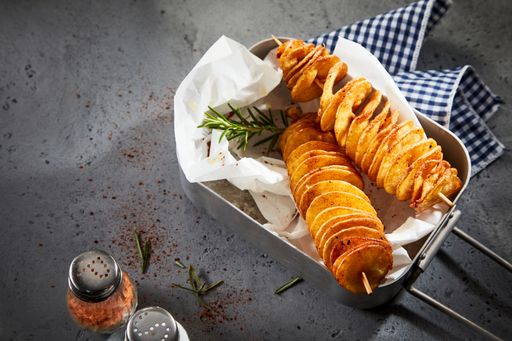 A high angle shot of delicious twist potatoes on skewers served with pepper and napkin on a gray table