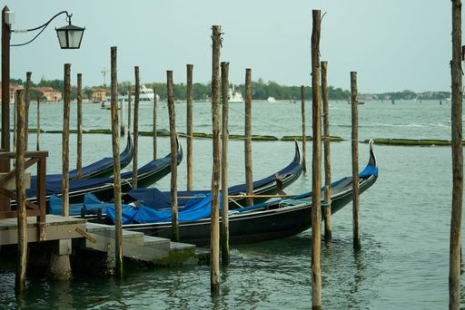 Gondolas moored at a wooden pier in Venice, Italy, with calm waters and a distant view of the city.