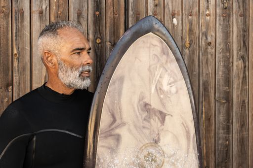 A portrait of a middle-aged African man in a surfing costume holding his surfing board and looking aside