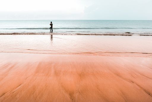 A shot of a young boy standing at the coastline washed by waves on a sandy beach