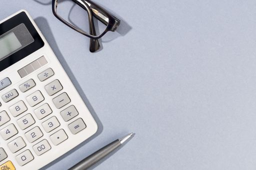 Flat lay of Calculator, pen and eyeglasses on gray background with Copy Space