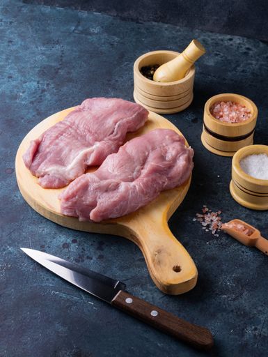 A vertical shot of row steak meat with seasonings on a wooden cutting board
