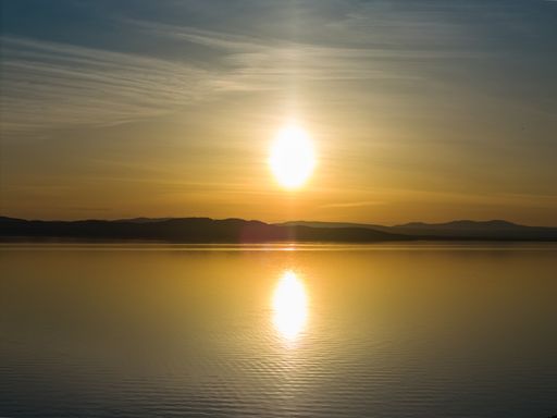 A serene sunset over a calm lake with distant hills and a golden sky reflecting on the water.