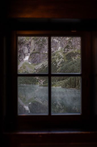 A vertical view of mossy rocks by the lake behind a window with wooden frames