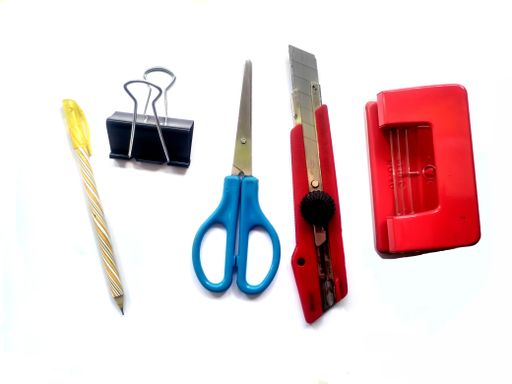 A pen, paper clip, a stapler, scissors, and a paper knife isolated on a white surface