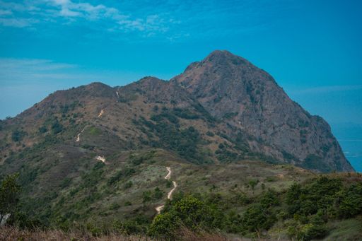 A scenic view of a rugged mountain landscape under a clear blue sky, featuring a winding hiking trail.