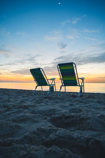 A vertical shot of a beautiful sandy beach with two deck chairs at sunset