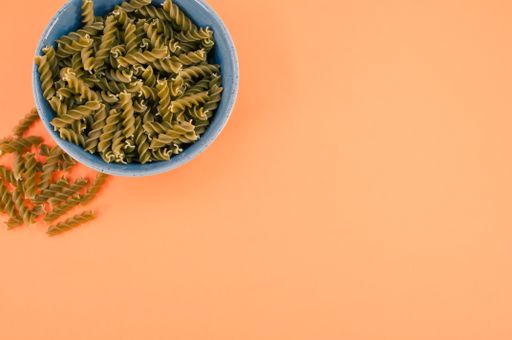 Vertical shot of  italian fusilli pasta in a blue bowl on an orange tabletop with text space