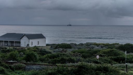 A house on the shore covered in greenery surrounded by the sea under a stormy sky