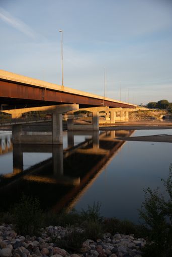 A vertical shot of a bridge that goes over the lake under the clear blue sky