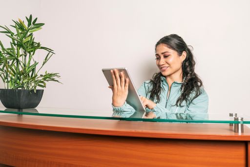 A young latina woman working at a reception with wooden furniture and a plant