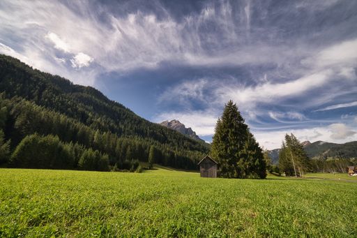 The cloudy blue sky over the green fields of Dolomite mountains in spring