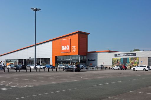 A bright orange B&Q building stands with cars parked out front in Trafford, UK.