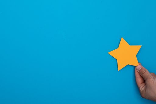 A top view of a hand holding a yellow paper star on a blue background. hotline helpdesk feedback concept