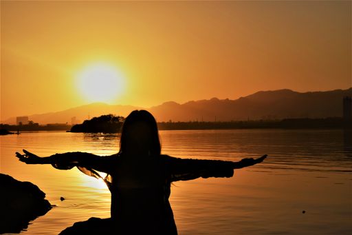 A silhouette of a person standing near a lake with open arms during a beautiful sunset in the evening