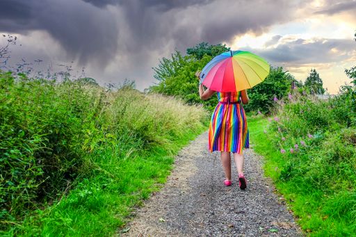 A rear view of a lady walking on a path wearing a multicolored dress holding a colorful umbrella