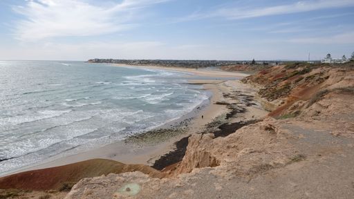 Scenic coastal view of a sandy beach with gentle waves and rocky cliffs under a partly cloudy sky at Port Noarlunga, South Australia.