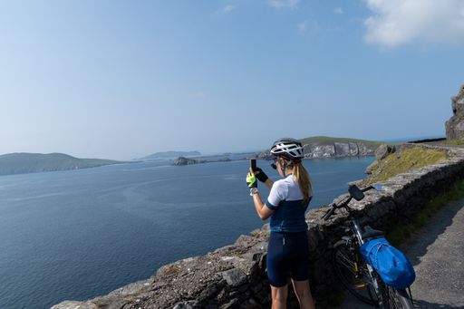 A shot of a Caucasian woman traveling by bicycle taking pictures with her smartphone at Dingle Peninsula, Ireland