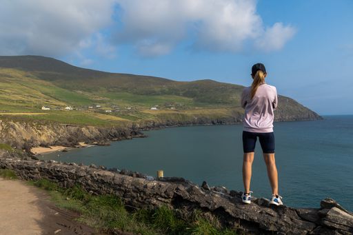 A shot of a young Caucasian woman standing on a stone wall looking at cliffs on Dingle peninsula, Ireland