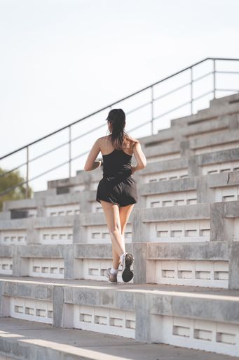 A vertical shot of a healthy adult Asian female running up on concrete stairs of the city stadium