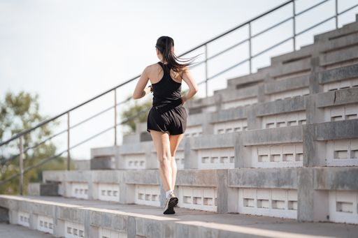 A healthy adult Asian female running up on concrete stairs of the city stadium