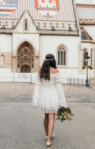 Back view of young bride wearing short wedding dress walking in street in front of St.Mark's church in Zagreb, Croatia.