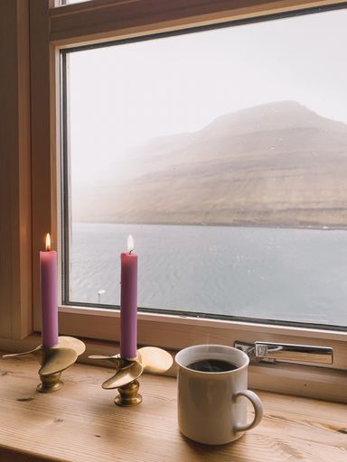 Candles and a cup of coffee on window, Scandinavian nature background. Faroe islands