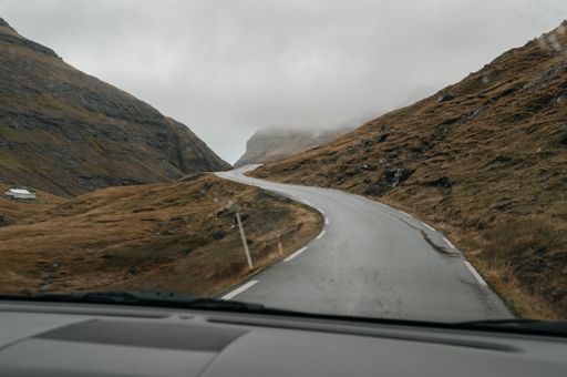 Driving in Faroe Islands. Scandinavian nature, brown fields and hills, moody sky. Gloomy Nordic landscape. Driving through empty road