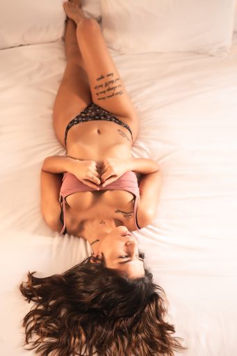 An attractive brunette Spanish woman with tattoos in a sensual pose on the bed