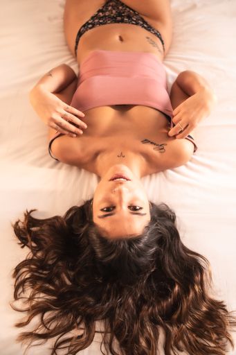 An attractive brunette Spanish woman with tattoos in a sensual pose on the bed