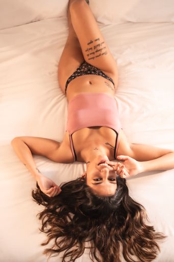 An attractive brunette Spanish woman with tattoos in a sensual pose on the bed