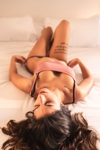 An attractive brunette Spanish woman with tattoos in a sensual pose on the bed