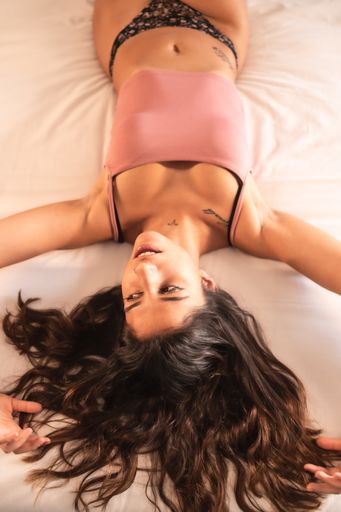 An attractive brunette Spanish woman with tattoos in a sensual pose on the bed